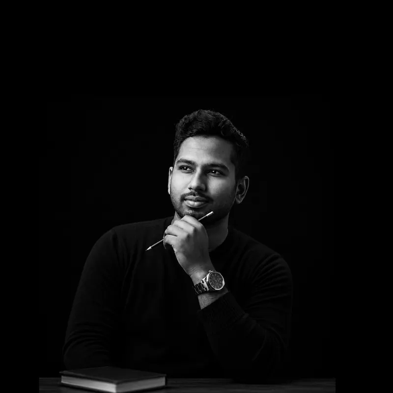 Black and white portrait of Sefat Khan looking thoughtful, holding a pen near his chin, with a book in front of him