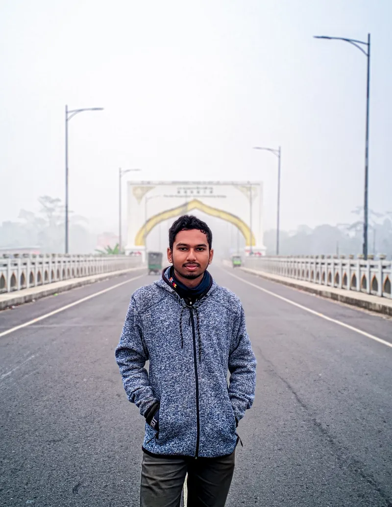 Sefat Khan standing on a bridge road in a grey-blue knit jacket on a hazy day