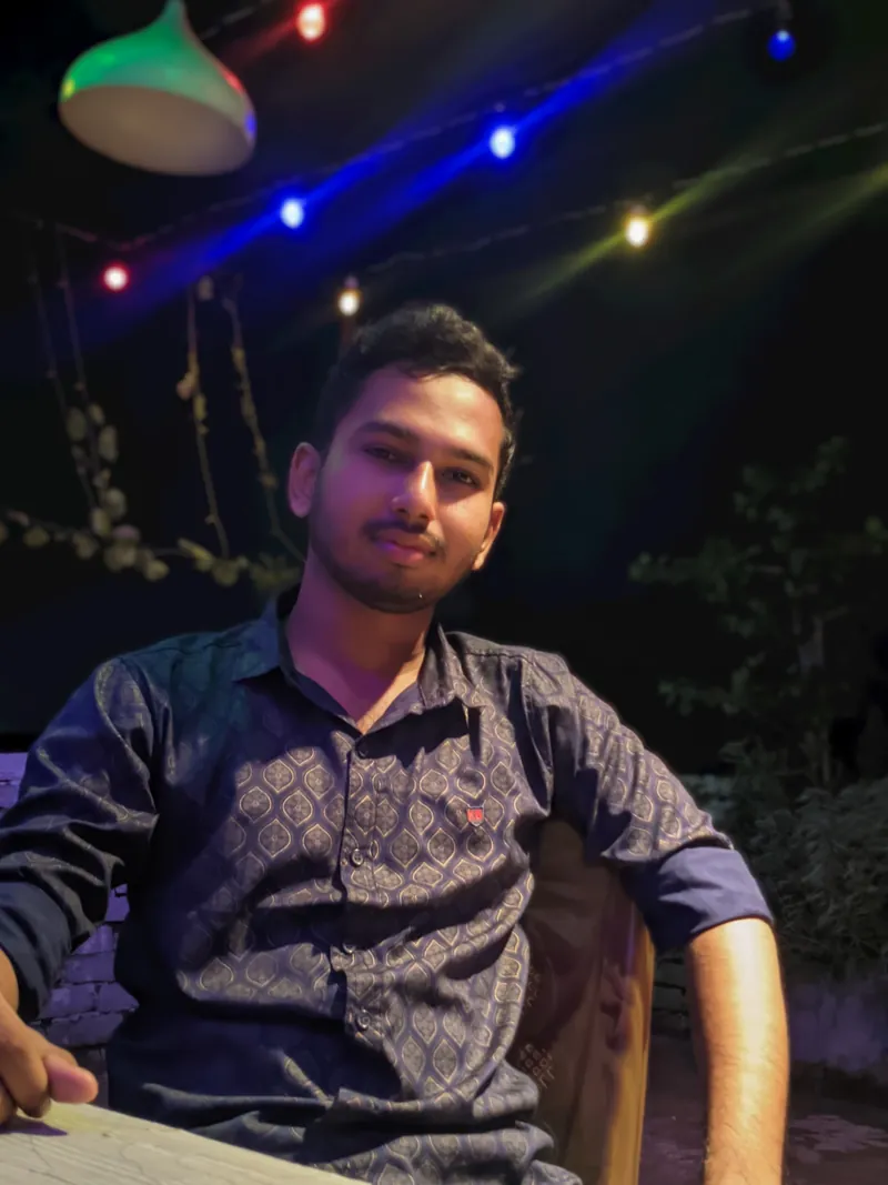 Sefat Khan seated in the evening with colourful string lights behind him