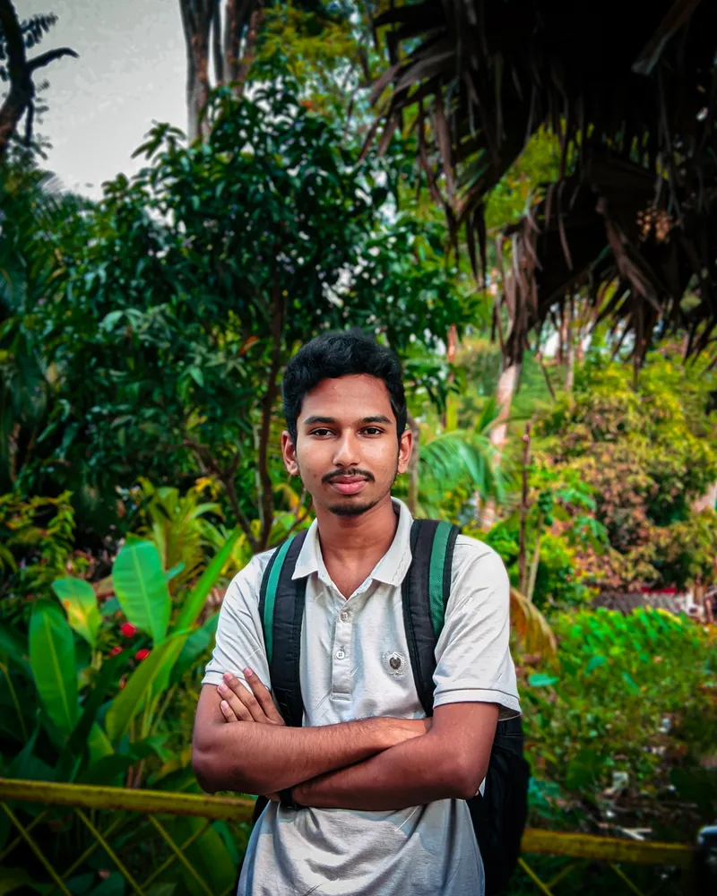 Sefat Khan with a backpack and arms crossed in a green garden