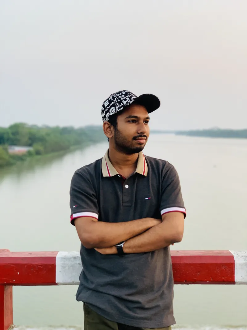 Sefat Khan wearing a cap and polo shirt beside a river with arms crossed