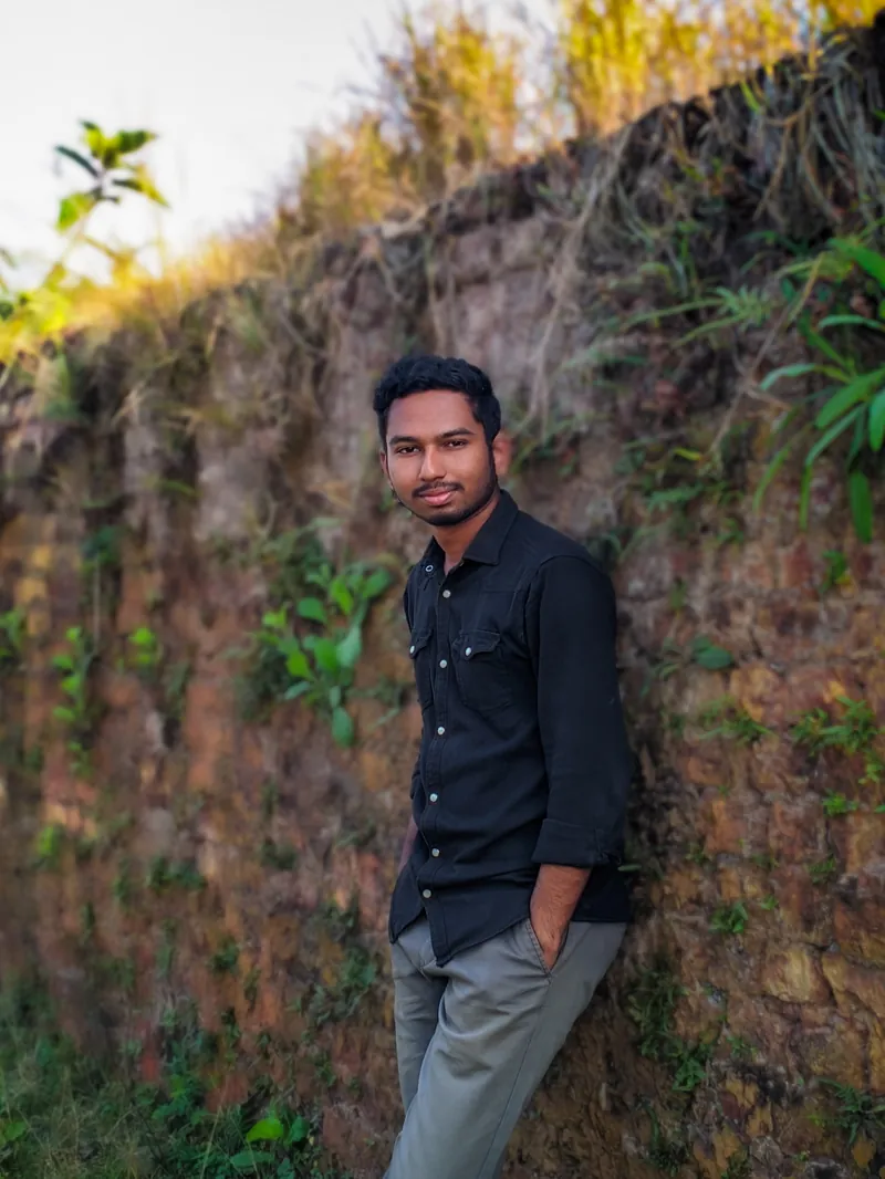 Sefat Khan in a dark shirt leaning against a mossy stone wall