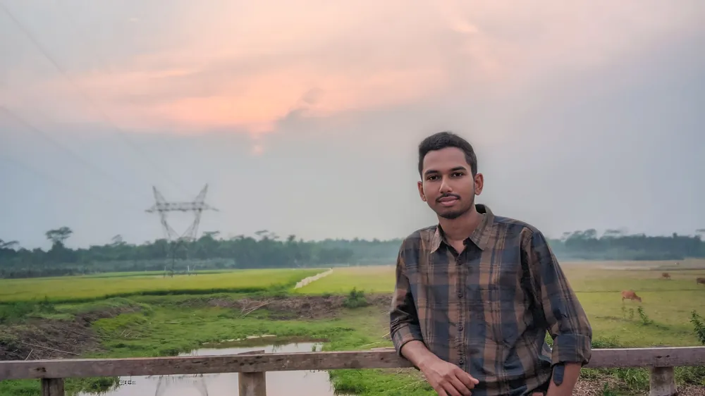 Sefat Khan in a checked shirt in open green countryside at sunset