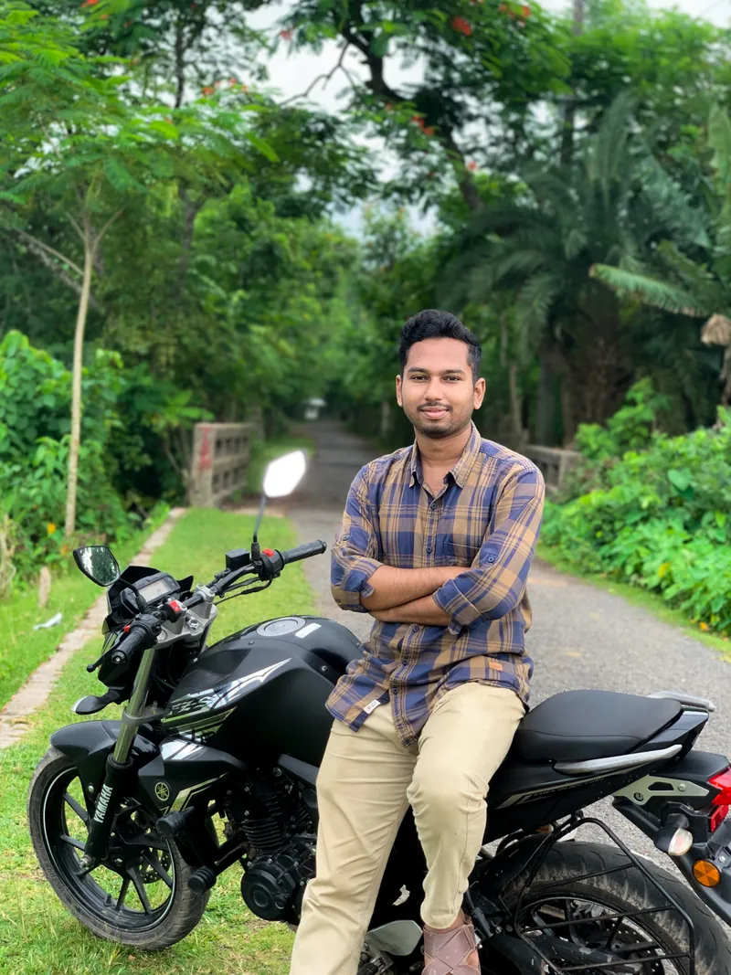 Sefat Khan sitting on a black motorbike on a green country road